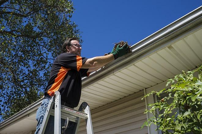 worker repairing damaged gutter on a residential roof in Amherst